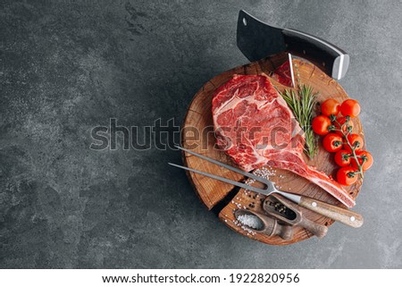 on a wooden block for meat a fresh raw tamahawk steak or a cowboy steak with a butcher's chopping ax for meat, next to it is a mixture of peppers and coarse salt, milled with thyme. fresh beef steak
