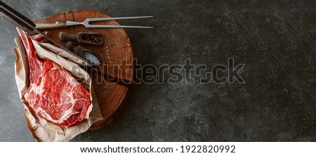 on a wooden block for meat a fresh raw tamahawk steak or a cowboy steak with a butcher's chopping ax for meat, next to it is a mixture of peppers and coarse salt, milled with thyme. fresh beef steak Royalty-Free Stock Photo #1922820992