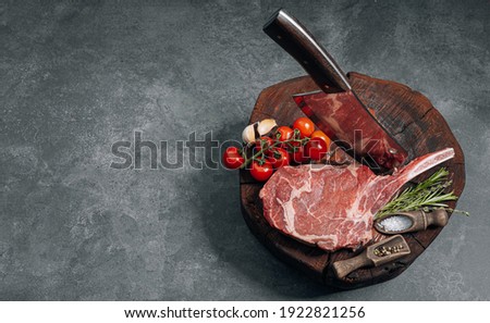 on a wooden block for meat a fresh raw tamahawk steak or a cowboy steak with a butcher's chopping ax for meat, next to it is a mixture of peppers and coarse salt, milled with thyme. fresh beef steak