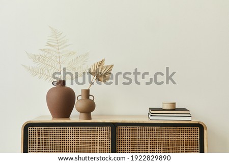 Modern scandinavian home interior with design wooden commode, dried leafs in ceramic vases and personal accessories in stylish home decor. Template. Copy space. White walls. Royalty-Free Stock Photo #1922829890