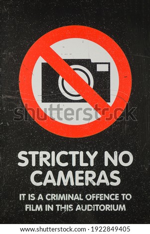 Strictly no cameras signage found in cinemas, theatres. Plastic face is scratched and covered with paint splashes.