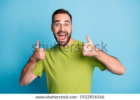 Photo of happy bearded brown haired young man show thumbs up wear glasses isolated on blue color background