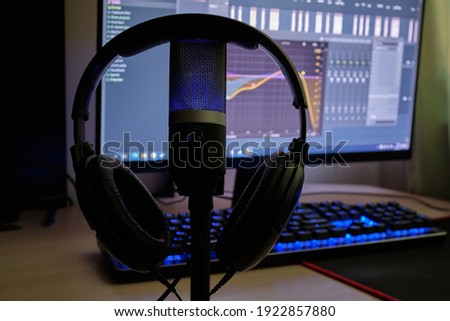 Blue microphone and headphones  at audio recording. Close-up. Microphone on the background of blurred computer screen. Microphone in the foreground. 