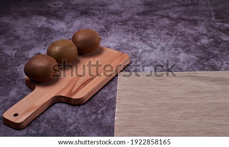 Three kiwis on a stone floor. Dark stone, front view, bright, brown tablecloth.