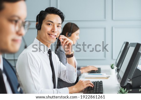 Asian call center team, customer service, telesales in formal suit wearing headset or headphone talking with customer in modern office Royalty-Free Stock Photo #1922861261