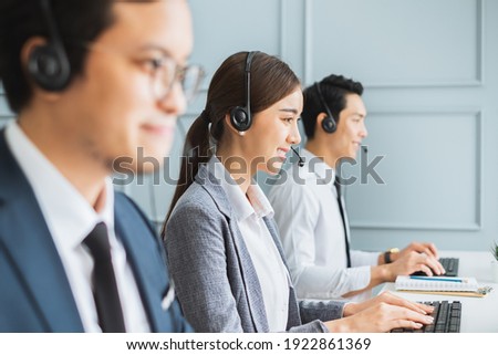 Asian call center team, customer service, telesales in formal suit wearing headset or headphone talking with customer in modern office Royalty-Free Stock Photo #1922861369