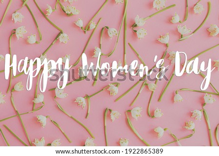 Happy women's day floral greeting card. Handwritten greetings on spring flowers border on pink paper flat lay. International women's day,  stylish floral congratulations