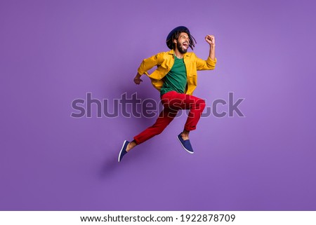 Full length photo of funky dark skin guy dressed yellow shirt headwear jumping running fast isolated purple color background Royalty-Free Stock Photo #1922878709