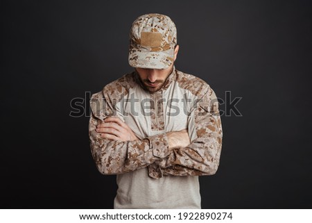 Close up of a handsome pensive young military man in uniform thinking isolated over black background