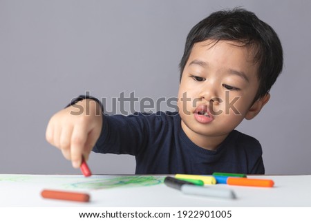 Asian boy is learning to paint with crayons on white paper.