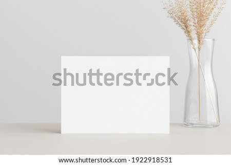 White invitation card mockup with a dried grass on a beige table. 5x7 ratio, similar to A6, A5. Royalty-Free Stock Photo #1922918531