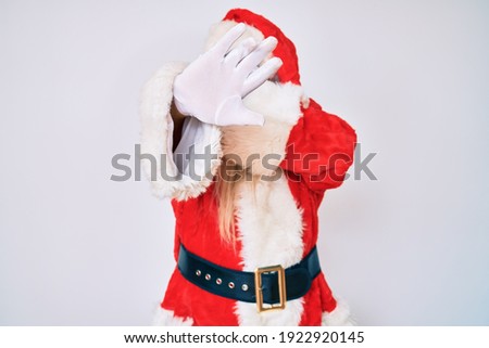 Old senior man with grey hair and long beard wearing santa claus costume with suspenders covering eyes with hands and doing stop gesture with sad and fear expression. embarrassed and negative concept