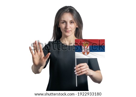 Happy young white woman holding flag of Serbia and with a serious face shows a hand stop sign isolated on a white background.