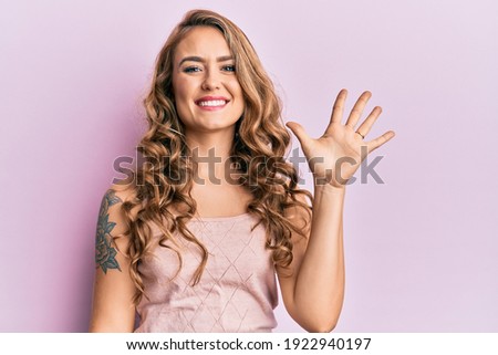 Young blonde girl wearing casual clothes showing and pointing up with fingers number five while smiling confident and happy. 