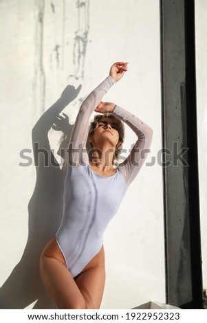 Girl in a bodysuit in the bright rays of the sun on the background of a light wall.
