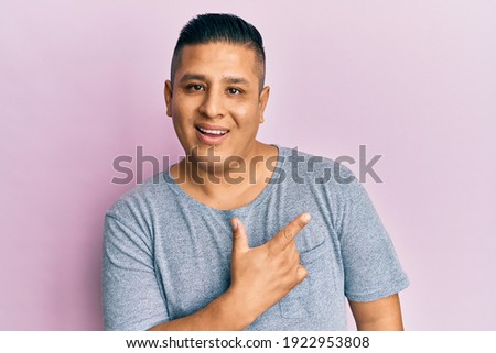 Young latin man wearing casual clothes smiling cheerful pointing with hand and finger up to the side 