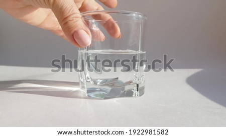 Close-up of female hand holding transparent glass with cold water on white background.