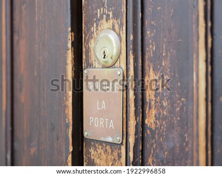 Wooden door, detail. Lock and plate written in Italian which recommends closing the door.
