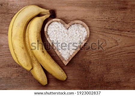 Wooden background with Ingredients and one portion of smoothies. empty copy space. bunch of ripe bananas, milk in a jug, oatmeal flakes in box in the form of heart.