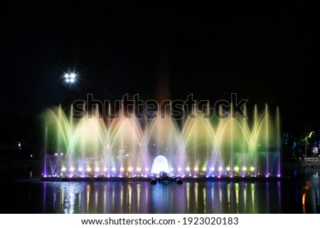 A dancing fountain or a fountain that is formed by controlling the ups and downs and has a light tone green bright and purple.  And the color reflecting on the water. Royalty-Free Stock Photo #1923020183