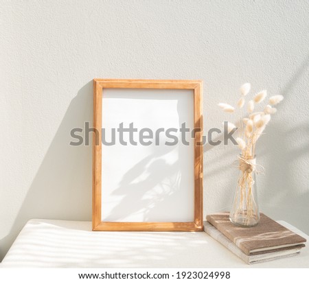 Blank mockup teak wood picture frame,craft book and dried flower in glass vase on beige table and cement wall background