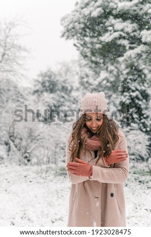 Glad female in warm clothes standing in snowy woods and looking down while enjoying winter weekend