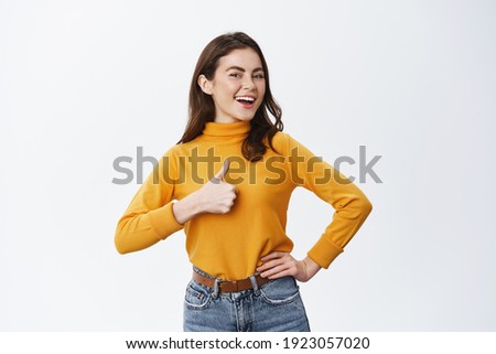 Excellent job. Smiling proud woman showing thumb up and say yes, nod to agree or approve, praising good work or nice choice, standing against white background. Royalty-Free Stock Photo #1923057020