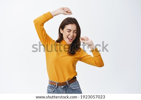 Happy attractive woman dancing and having fun, raising hands up carefree, enjoying music, standing against white background.