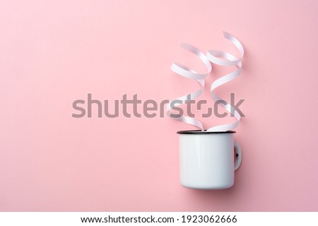 White metal cup on pink background with ribbons