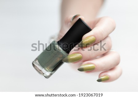 Woman's hand with long nails and light and dark green manicure with bottles of nail polish.	