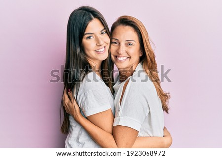 Beautiful hispanic mother and daughter smiling happy hugging over isolated pink background. Royalty-Free Stock Photo #1923068972