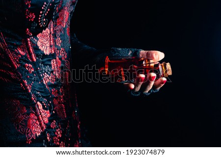 Someone wearing a black and red corset and black lace gloves holding two glass stopper bottles with red liquid