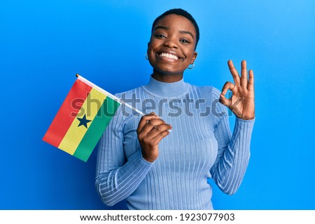 Young african american woman holding ghana flag doing ok sign with fingers, smiling friendly gesturing excellent symbol 