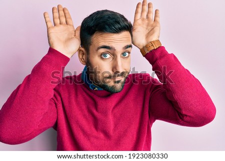 Young hispanic man wearing casual clothes doing bunny ears gesture with hands palms looking cynical and skeptical. easter rabbit concept. 