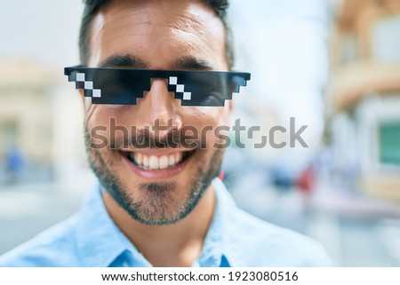 Young hispanic man smiling happy wearing funny sunglasses standing at street of city.