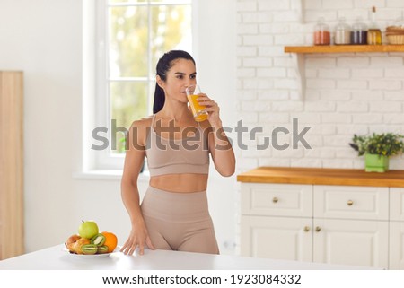 Morning routine. Beautiful fitness woman in sportswear drinks fresh fruit juice after workout standing at home in the kitchen. Concept of a healthy diet and vitamins. Royalty-Free Stock Photo #1923084332