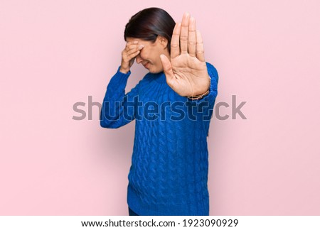 Young hispanic woman wearing casual clothes covering eyes with hands and doing stop gesture with sad and fear expression. embarrassed and negative concept. 