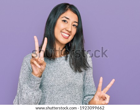 Beautiful asian young woman wearing casual clothes smiling looking to the camera showing fingers doing victory sign. number two. 