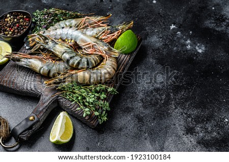 Raw black tiger prawns, shrimps and spices. Black background. Top view. Copy space