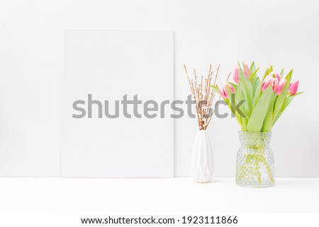 Home interior with decor elements. Mockup with a white canvas and pink tulips in a vase on a light background