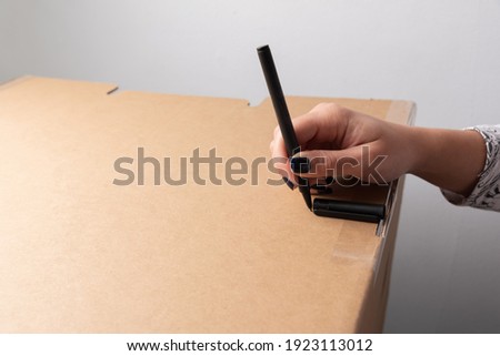 Female hand marks distance with pen marker on cardboard box for further cutting with craft knife and opening a window of light with copy space