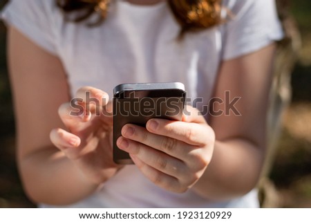 irreconcilable girl's hands using mobile phone outdoors with white T-shirt Royalty-Free Stock Photo #1923120929