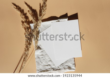 A blank greeting card, desaturated mock up. Two empty sheets of white paper on a linen towel on pastel surface and yellow wheat spikes 