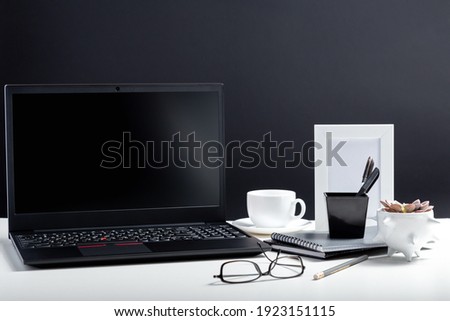 Home Office laptop blank template display workspace. Desktop with laptop pc smart phone, notepads pens office suppliers cup of coffee drink plant flower. White work desk table on black background