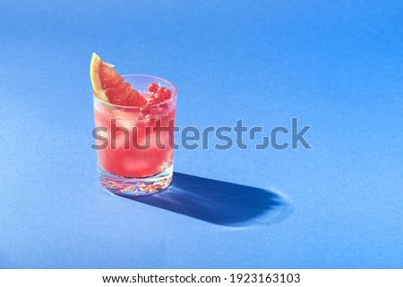 Tropical fruit summer coctail with red grapefruit, berries and ice on blue background. Minimal cold drink layout.