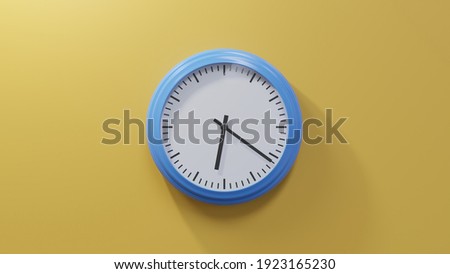Glossy blue clock on a orange wall at twenty-one past six. Time is 06:21 or 18:21