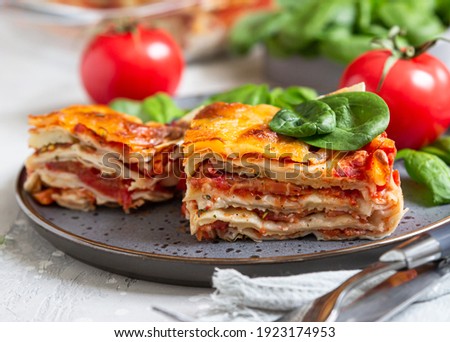 Italian lasagna with tomato sauce and cheese served with tomatoes and spinach, light concrete background. Homemade vegetarian lasagna. Selective focus. Royalty-Free Stock Photo #1923174953