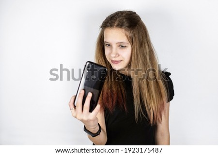 A young teen girl admires herself by looking at her phone like in a mirror, she tries to take a quality selfie photo to promote her account on social networks. Copy space