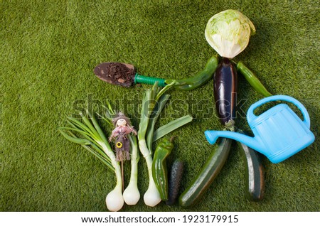 concept of a doll made of vegetables with a blue watering can, a
a cultivation shovel  and other vegetables on the left.