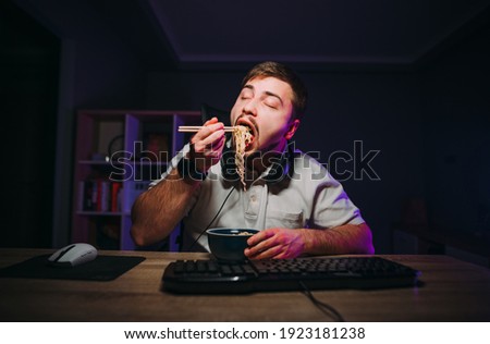 Hungry man eats Asian food with chopsticks at night between work. Freelancer works at night on the computer and eats fast food.